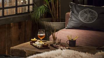 A cozy room with a large window, a plush sofa, a wooden table with snacks and drinks, and a large plant.