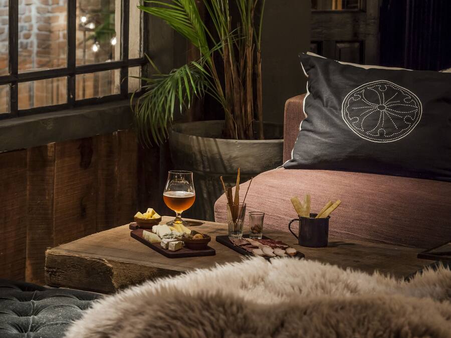 Ein gemütliches Zimmer mit großem Fenster, einer bequemen Couch, einem Holztisch mit Snacks und Getränken sowie einer großen Pflanze.
