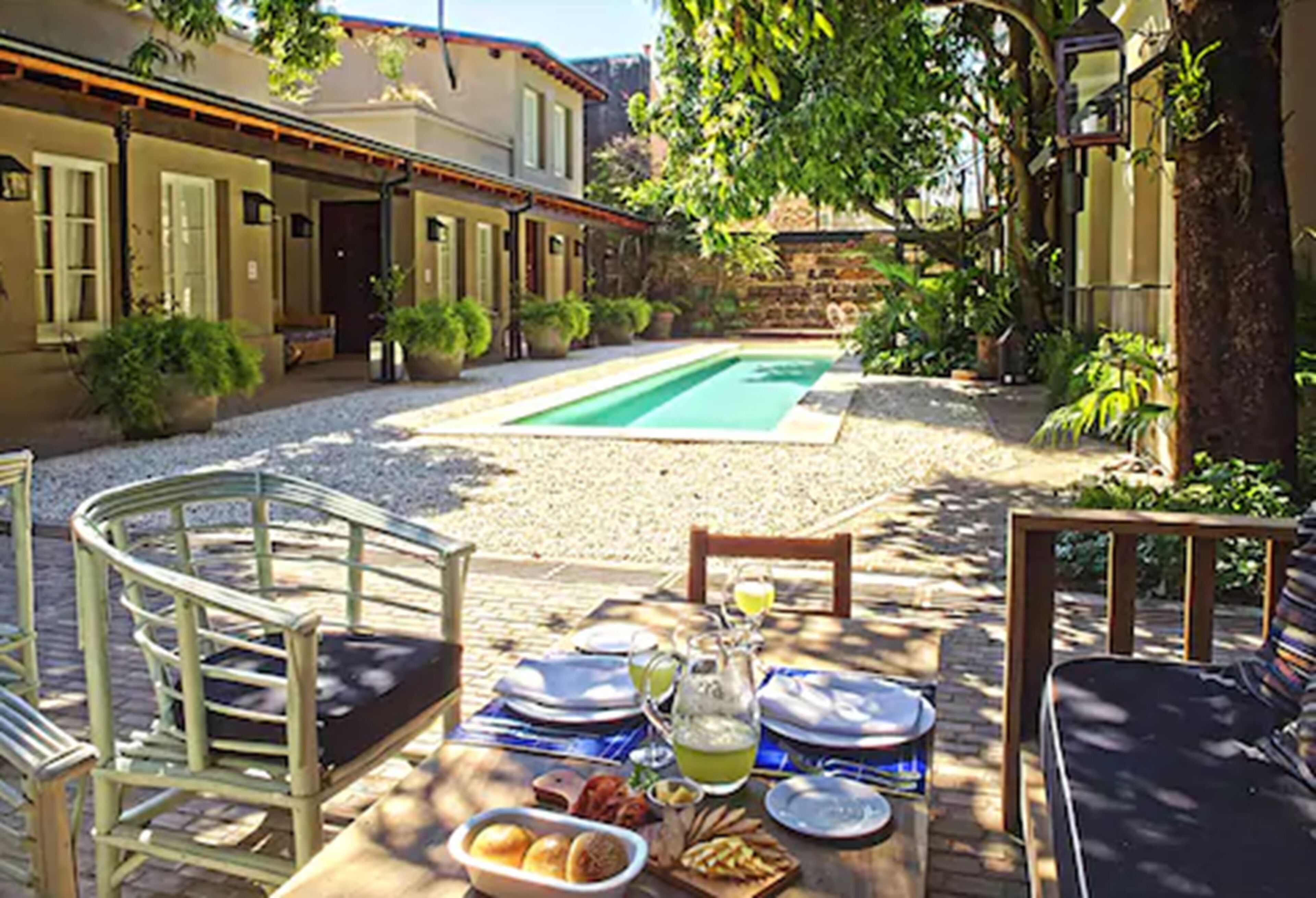 A dining table set outdoors with chairs, a pool, and a building in the background.