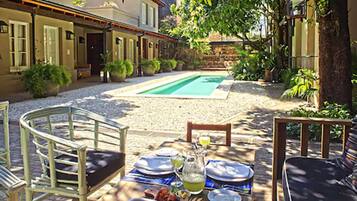 A dining table set outdoors with chairs, a pool, and a building in the background.