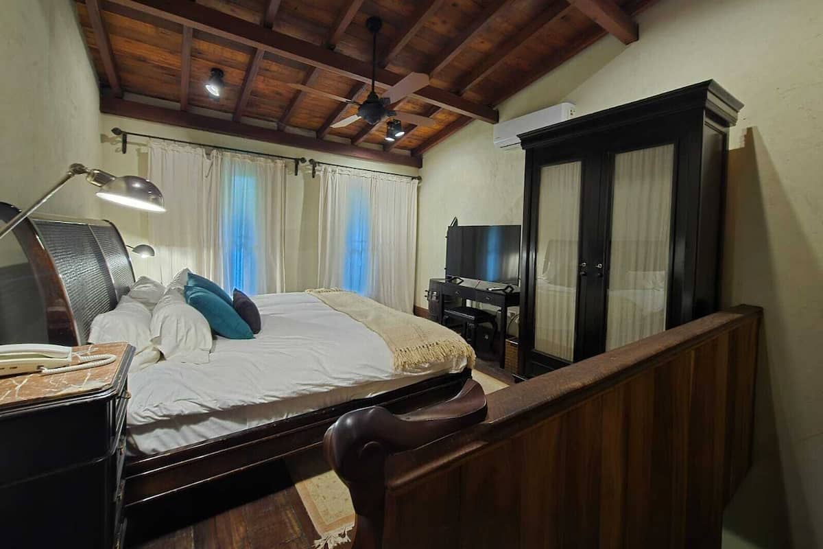 A bedroom with a bed, a desk with a computer, a wardrobe, and a ceiling fan.