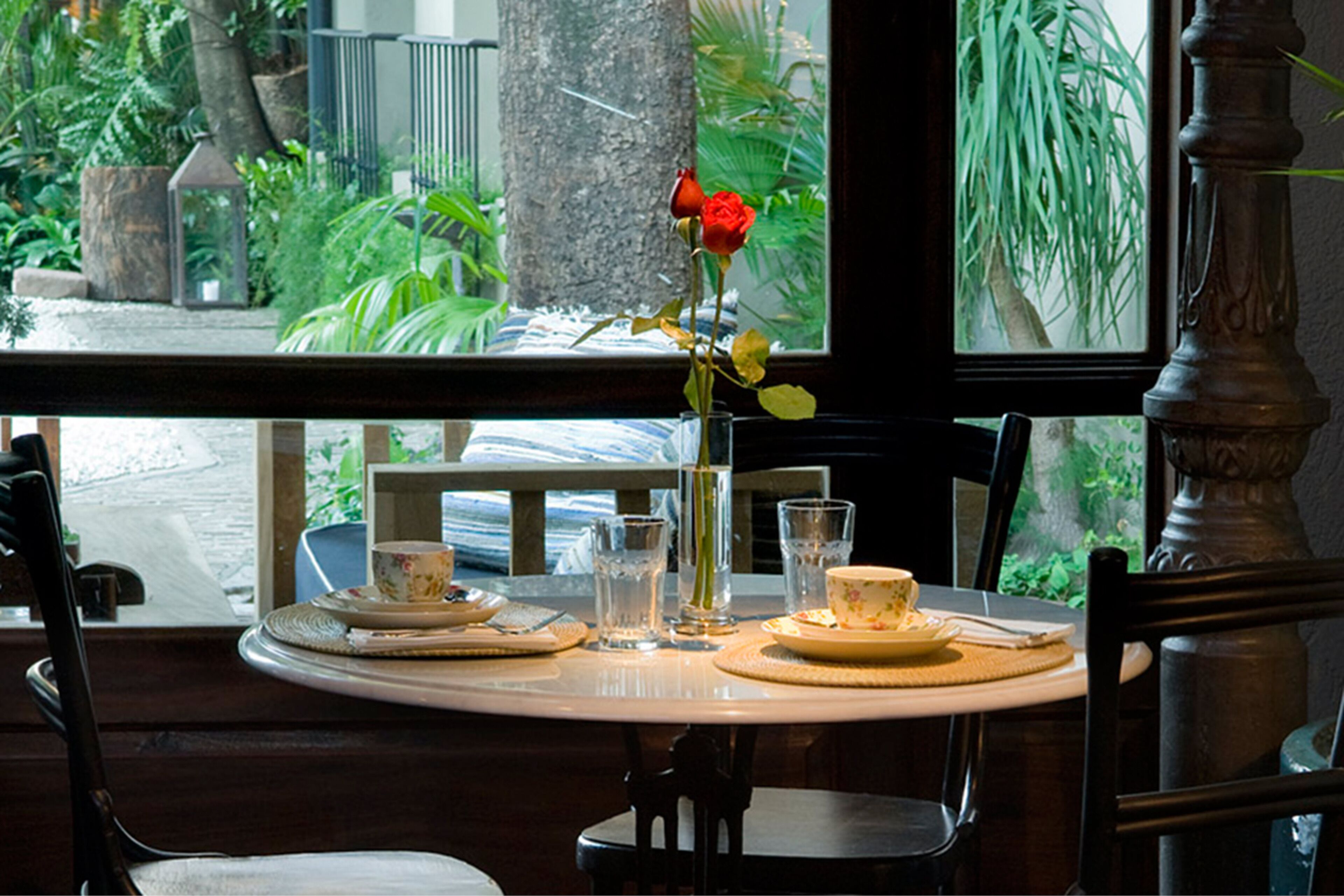 Una mesa de comedor dispuesta con platos, vasos y un florero con una flor.