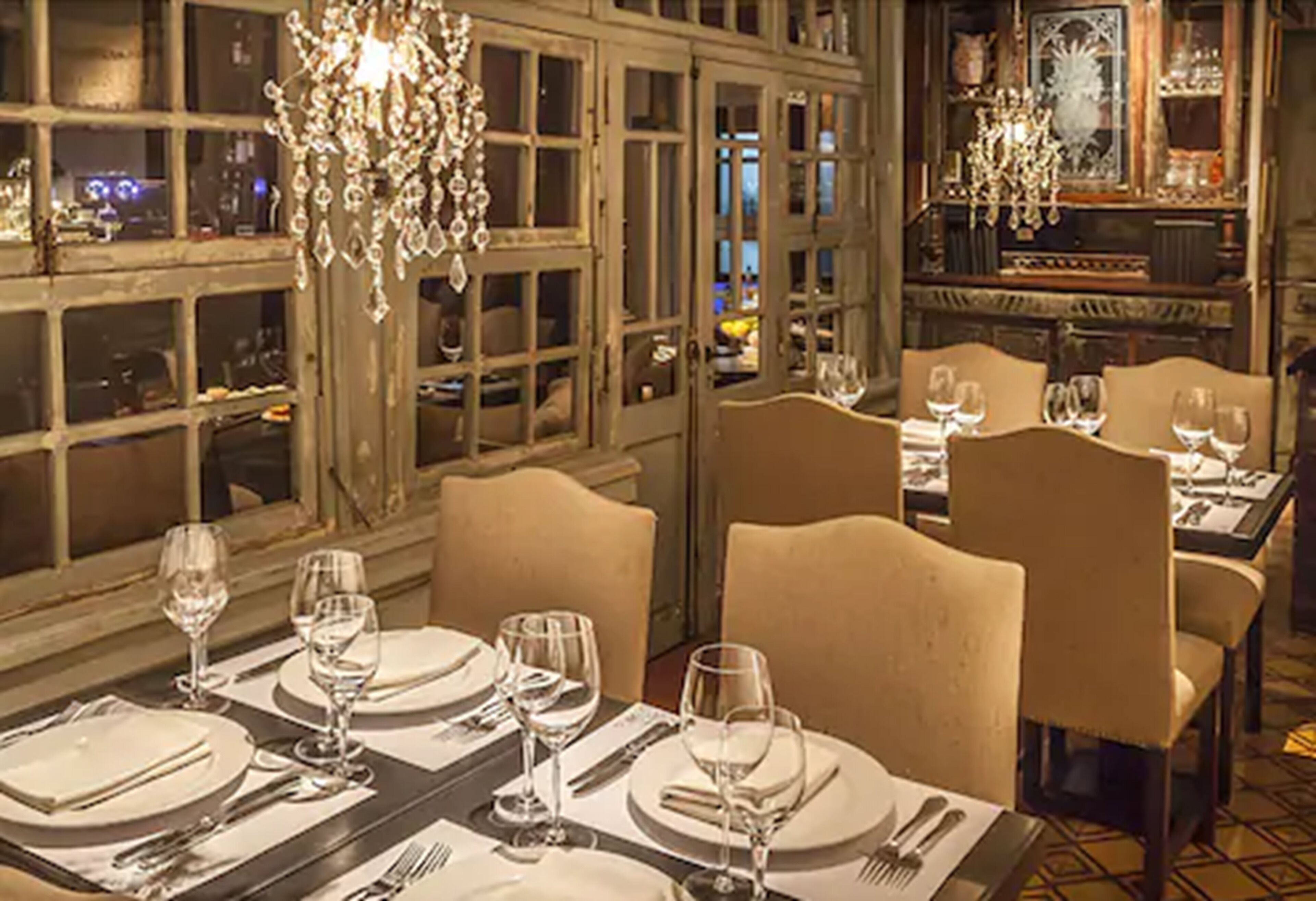 Un restaurant où les tables sont dressées pour le service, agrémenté de lustres et offrant une vue sur l’extérieur grâce à de grandes fenêtres.