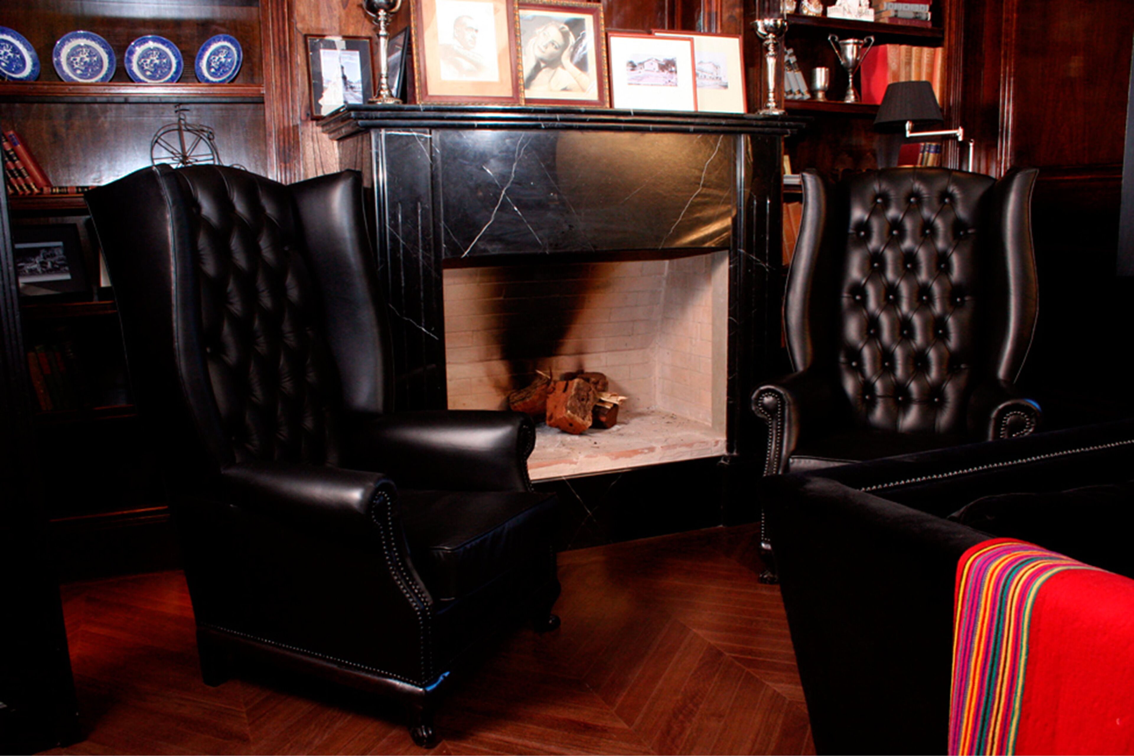 A room with a fireplace, two leather armchairs, and a red sofa.