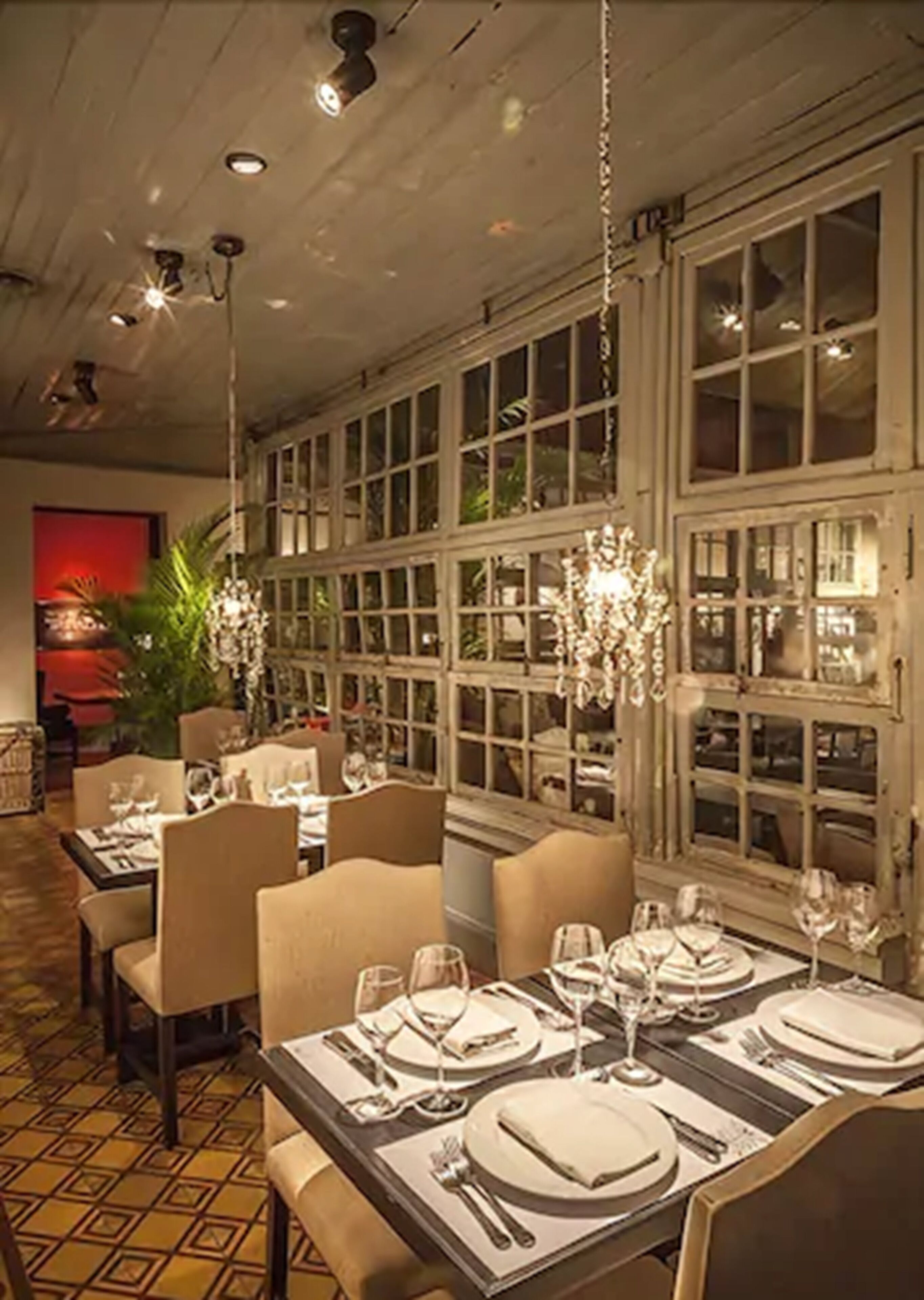 En restaurant med dækketøjsdækkede borde, store vinduer og hængende lysekroner.