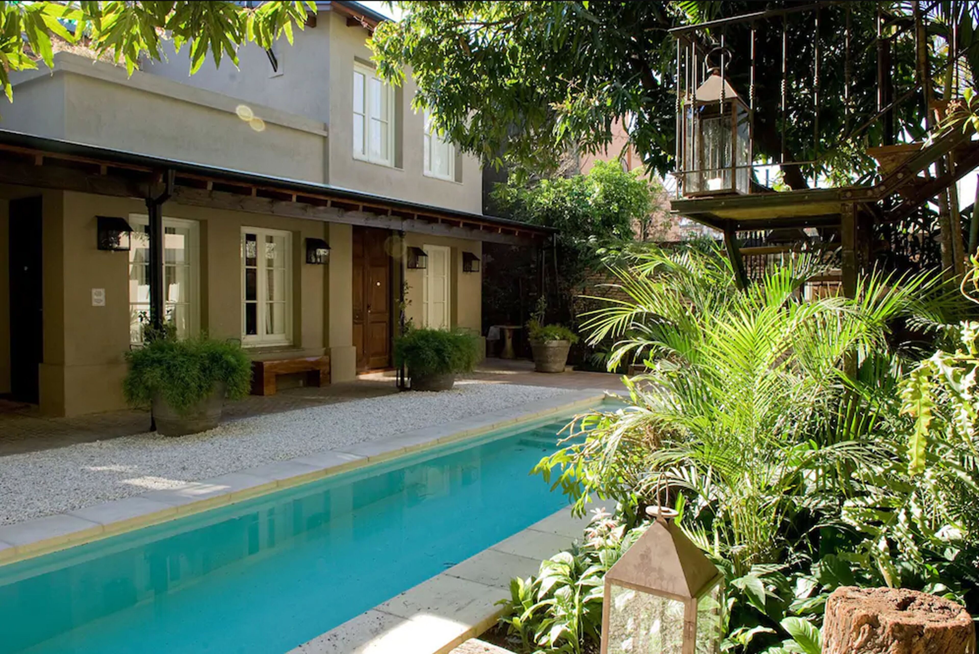 Un área de piscina con un edificio, plantas en macetas y una terraza de madera.