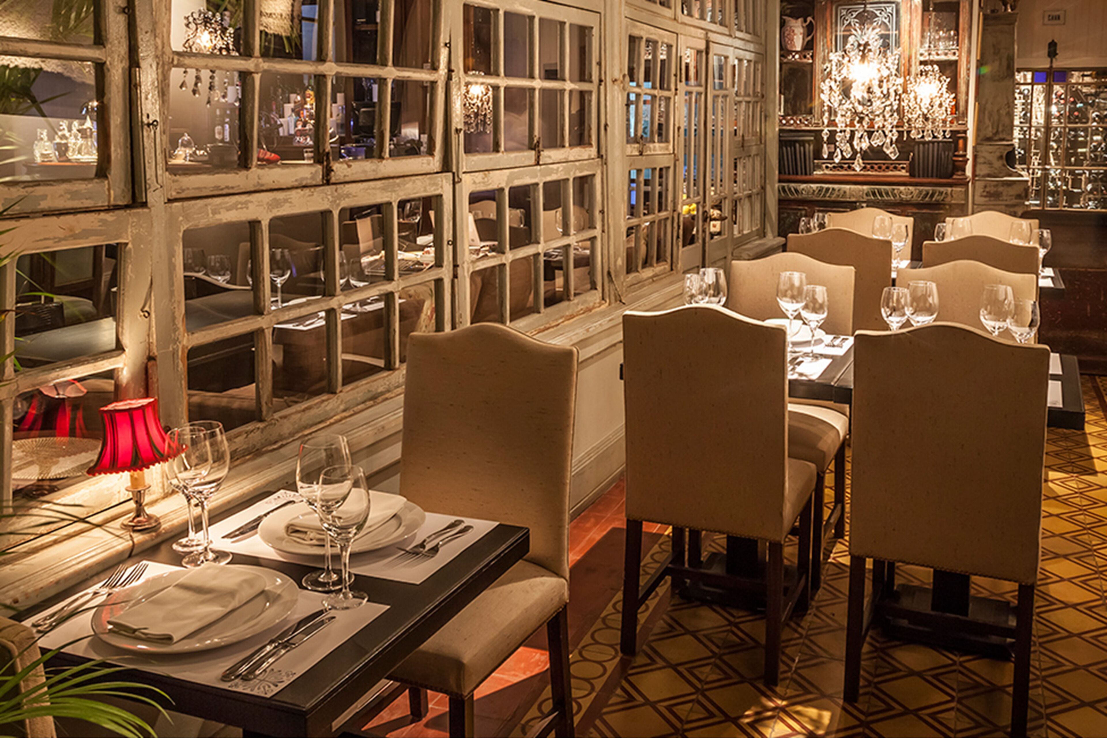 A restaurant with multiple tables set for dining, each with chairs, plates, cutlery, and wine glasses.