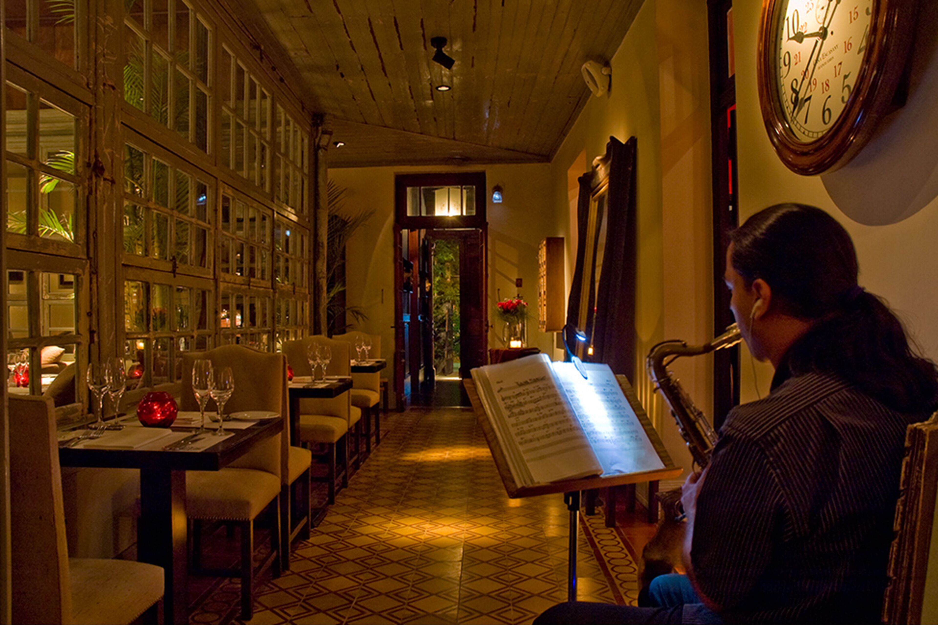 A restaurant with a long table set for dining, a menu stand, and a clock on the wall.