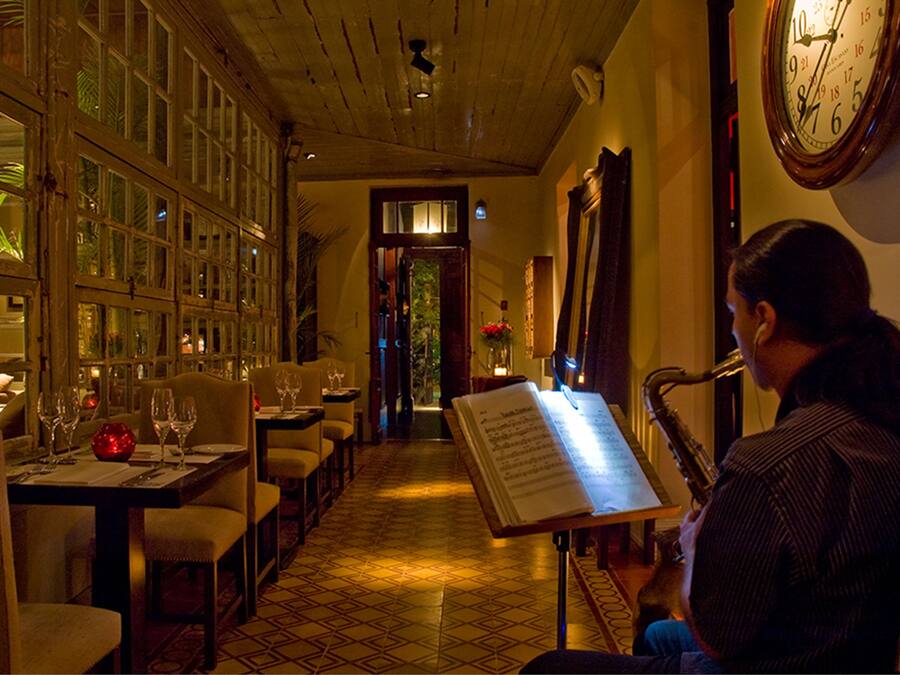 A restaurant with a long table set for dining, a menu stand, and a clock on the wall.