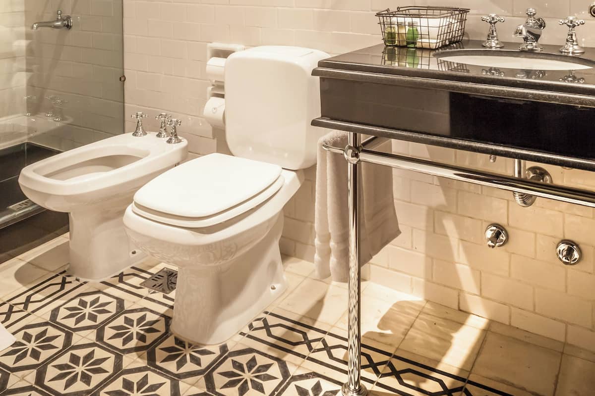 A bathroom with a shower, two toilets, a sink, and a mirror.