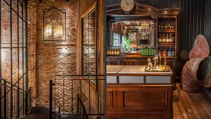 Een bar met een houten toonbank, een klok en flessen op planken.