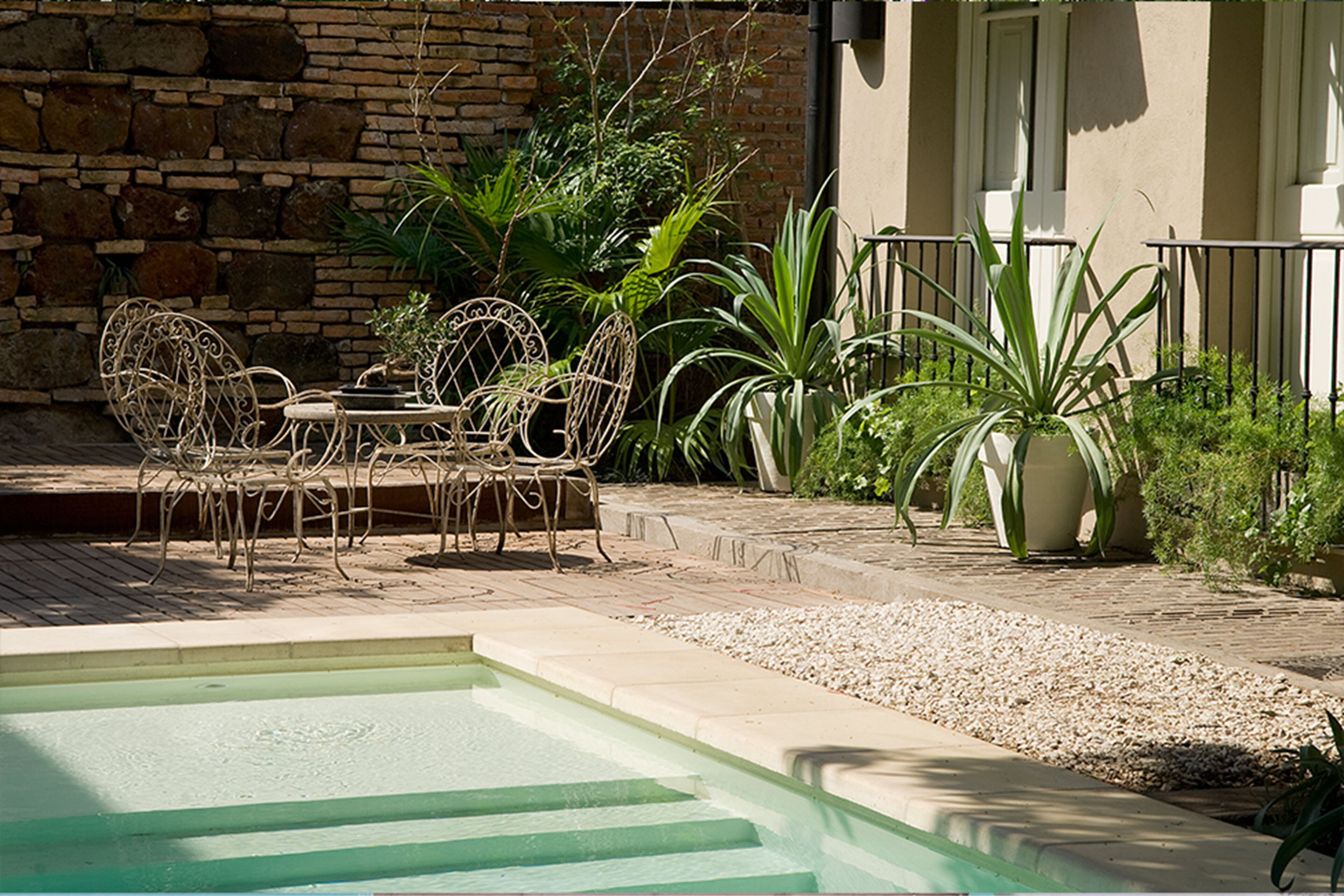 A pool area with a stone wall, metal chairs, and potted plants.