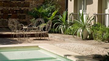 A pool area with a stone wall, metal chairs, and potted plants.