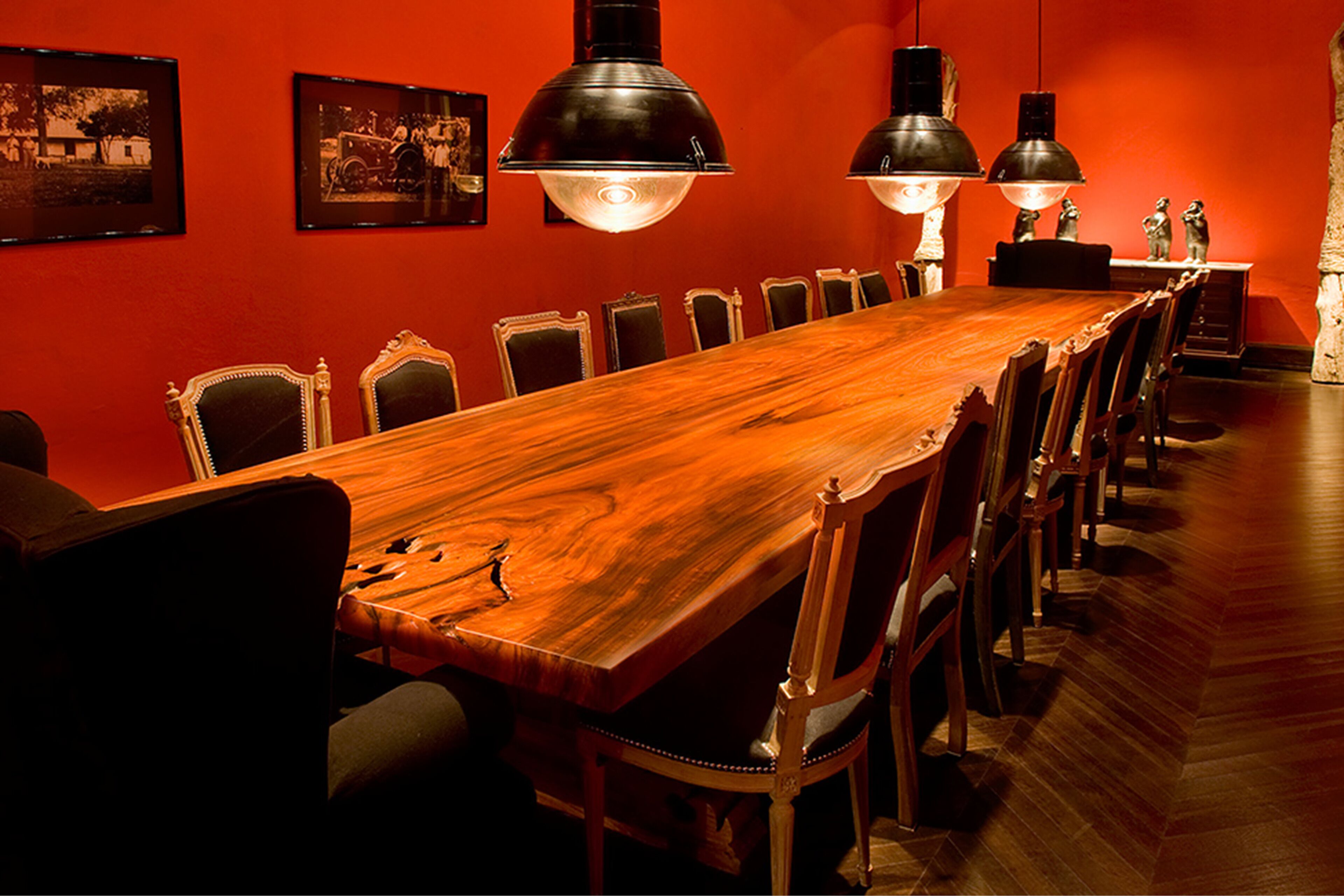 A long wooden conference table with chairs, black pendant lights, and framed pictures on the wall.