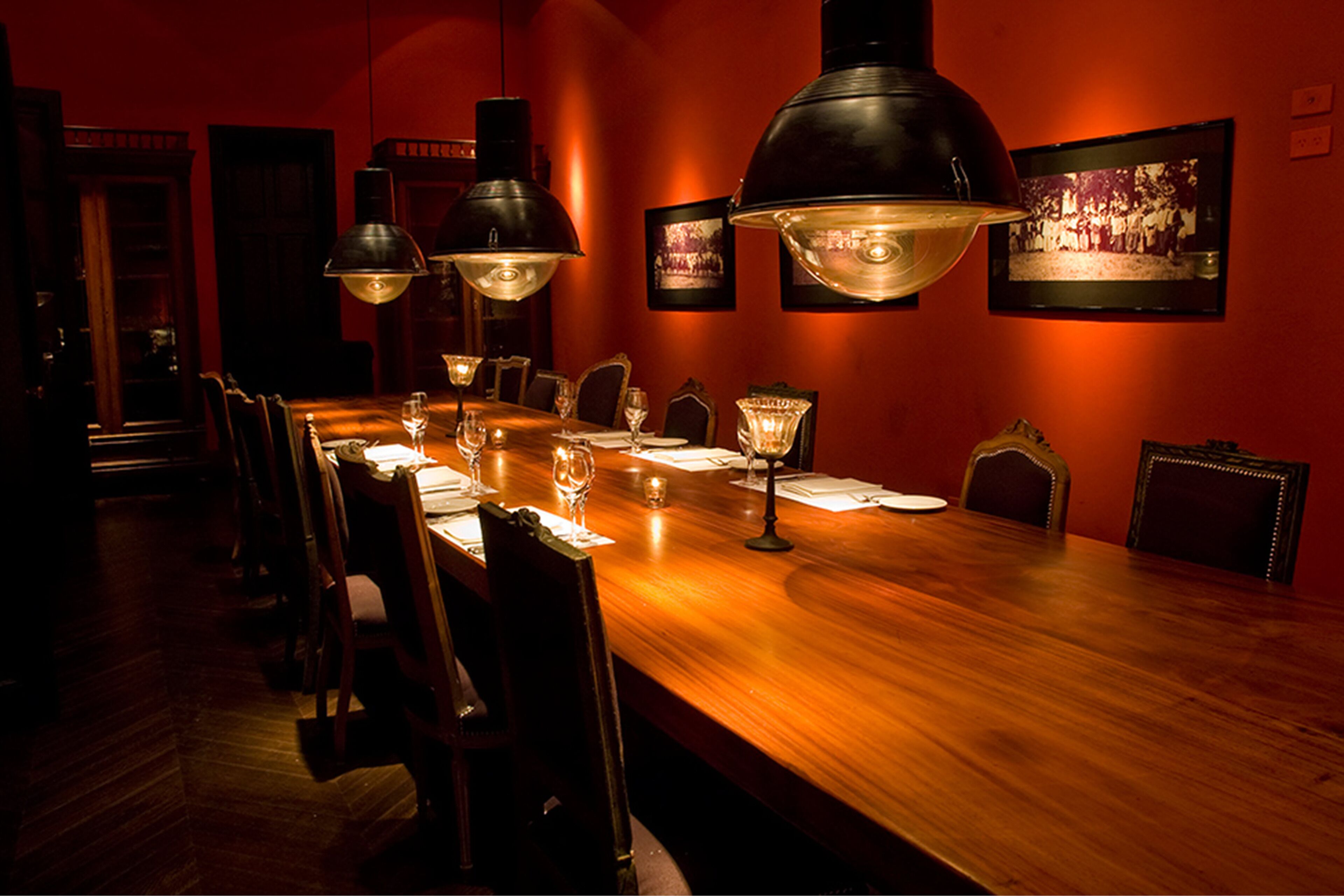 Una larga mesa de comedor de madera con sillas, iluminada por tres grandes lámparas colgantes.