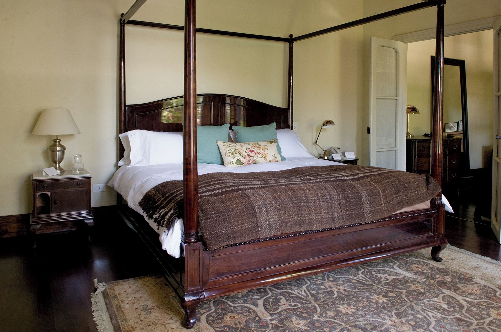 A four-poster canopy bed with a wooden frame, a nightstand with a lamp, and a patterned rug.
