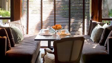 A cozy seating area with a table set for breakfast, featuring a bowl of fruit, cups, and a glass of water.