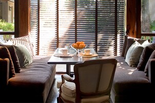 Un rincón acogedor con una mesa lista para el desayuno, que incluye un cuenco de fruta, tazas y un vaso de agua.