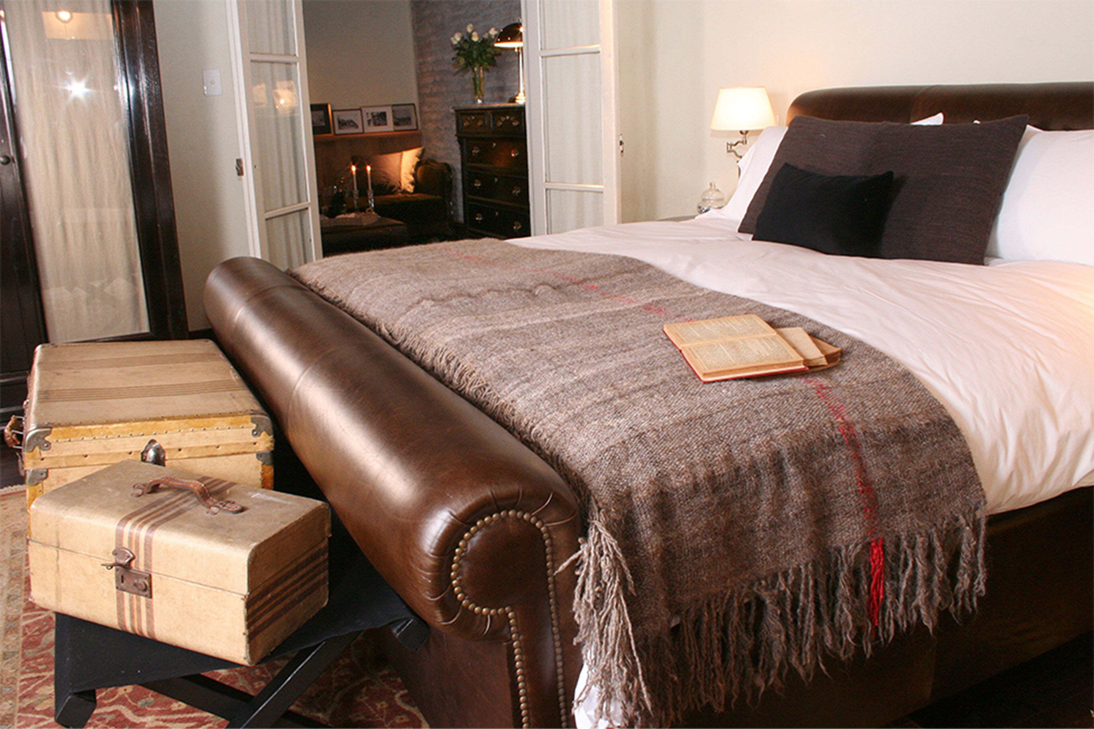 A bedroom with a large bed, a wooden bench, and two vintage suitcases.