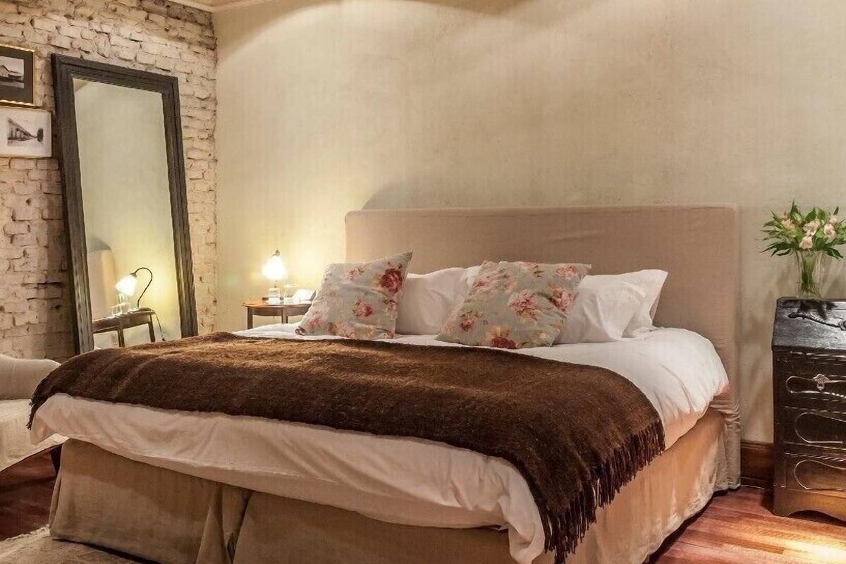 A bedroom with a wooden ceiling fan, a large bed with floral pillows, a nightstand with a lamp, and a stone wall.