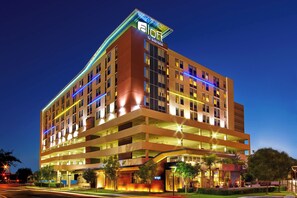 A multi-story hotel with a prominent sign at the top, multiple balconies, and a well-lit entrance area. - Aloft by Marriott Houston by the Galleria (Houston)