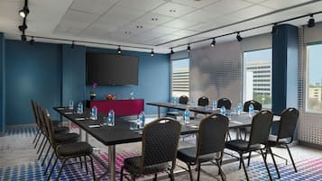 Een vergaderzaal met een grote tafel, stoelen, een flatscreen-televisie en uitzicht op de stad.