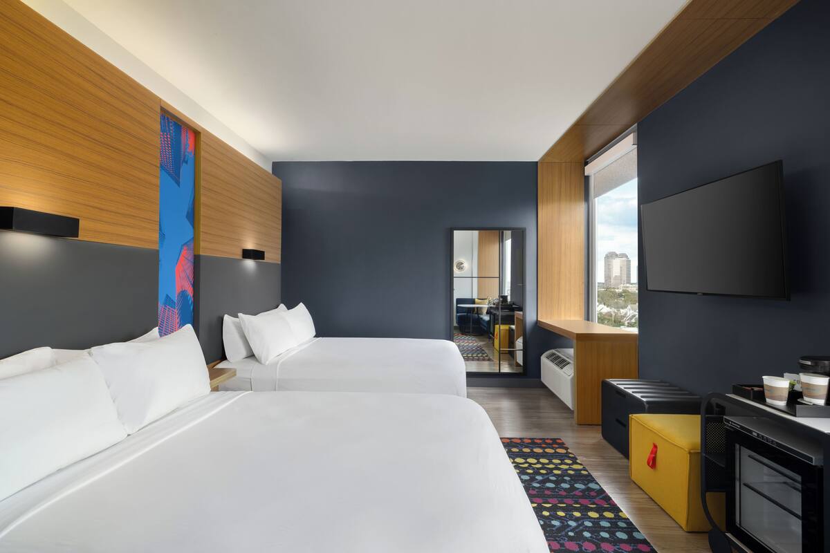 Habitación de hotel con dos camas, televisión, escritorio con computadora y vista a la ciudad.
