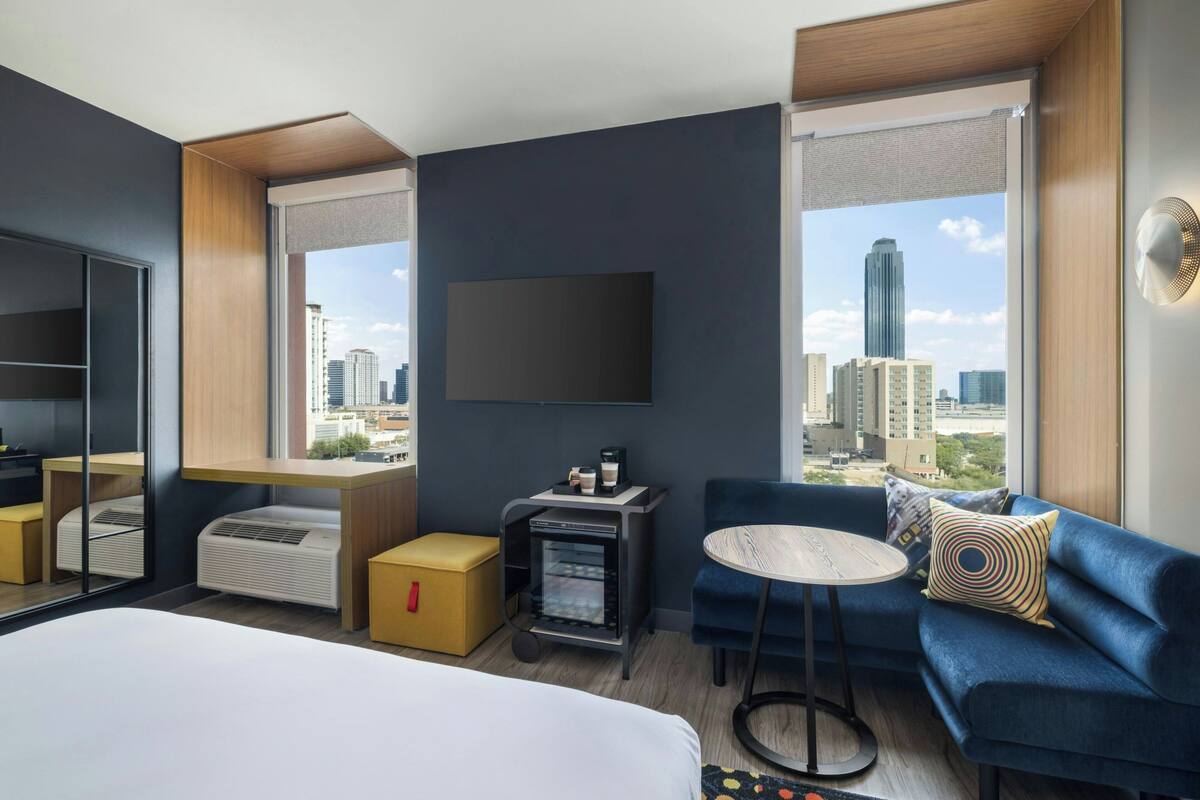 Una habitación de hotel moderna con cama, sofá, una mesita, televisor y vistas a la ciudad.