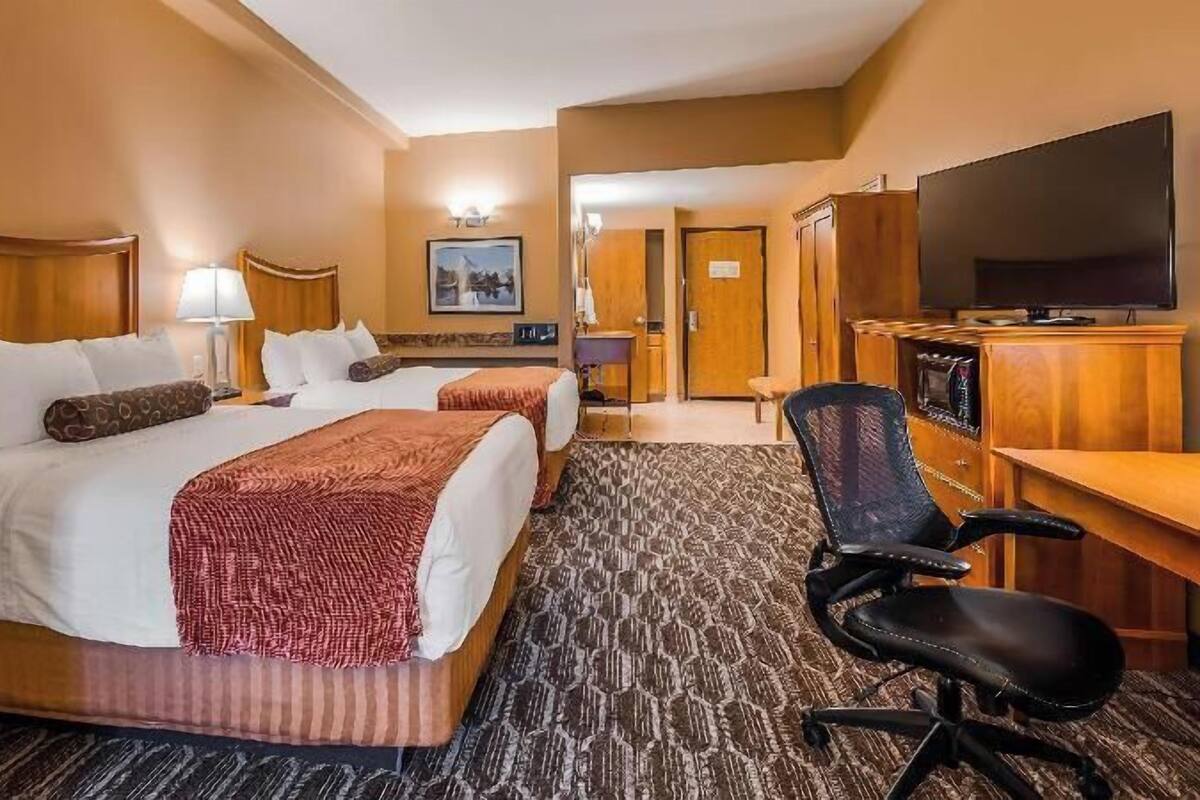 Een hotelkamer met twee bedden, een bureau met stoel, een televisie en een tapijtvloer.