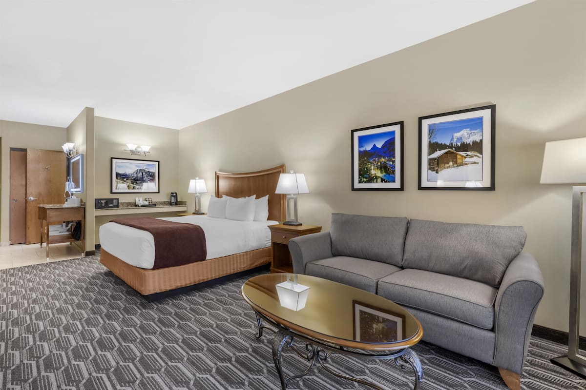 Een hotelkamer met een bed, een bank, een bijzettafeltje, een bureau en twee ingelijste foto's aan de muur.