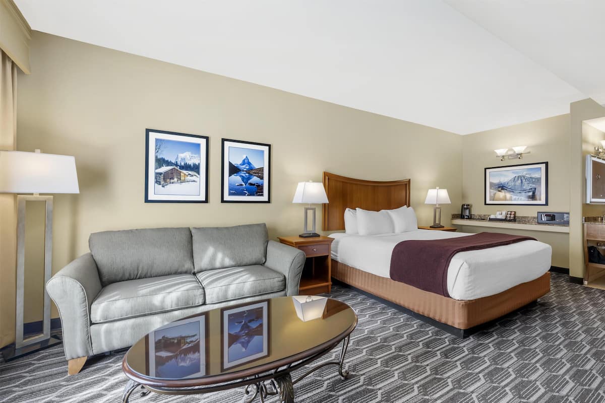 Een hotelkamer met een bed, een grijze bank, een kleine tafel en twee foto’s in lijsten aan de muur.