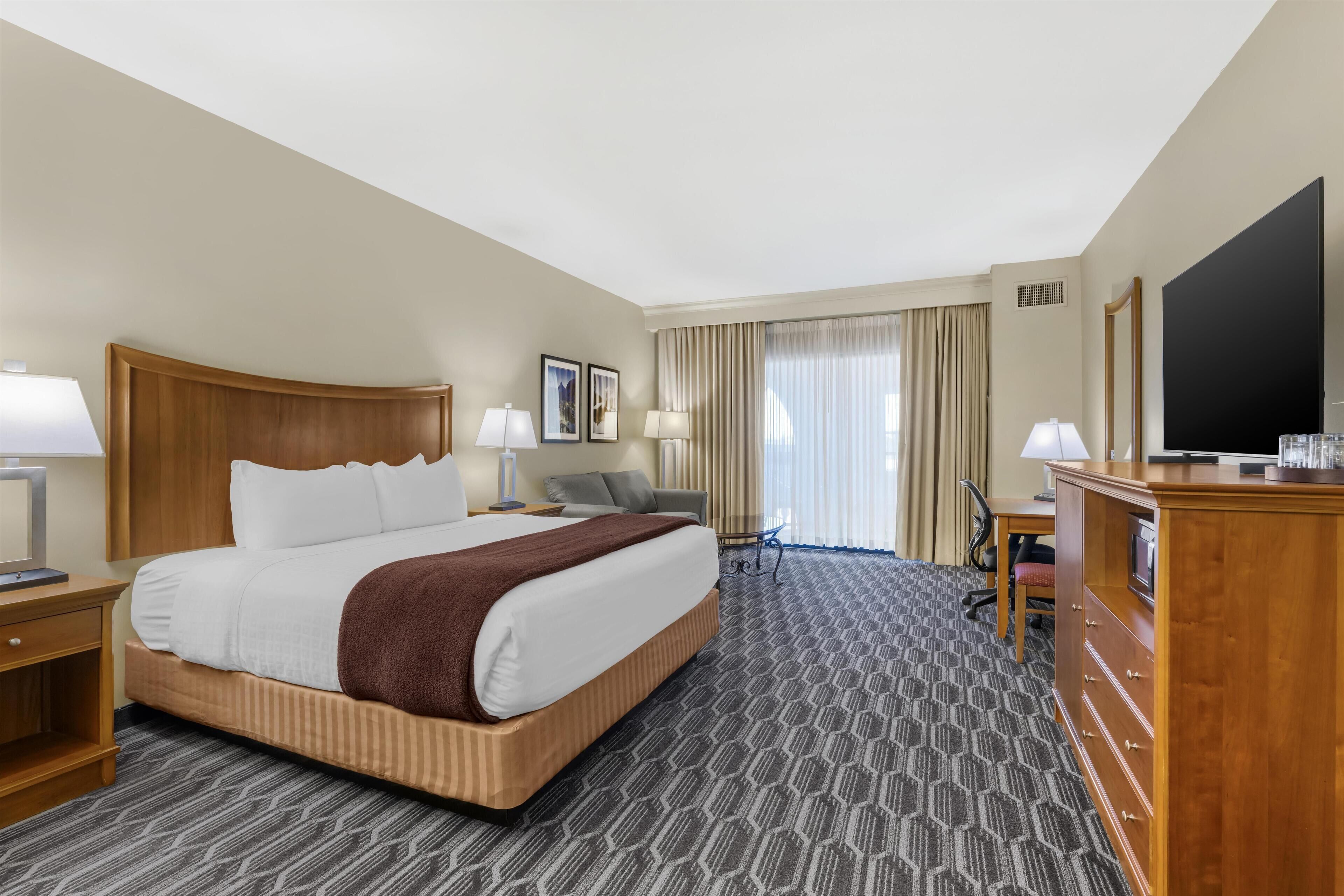 A hotel room with a large bed, a desk, a chair, a TV, and a wardrobe.