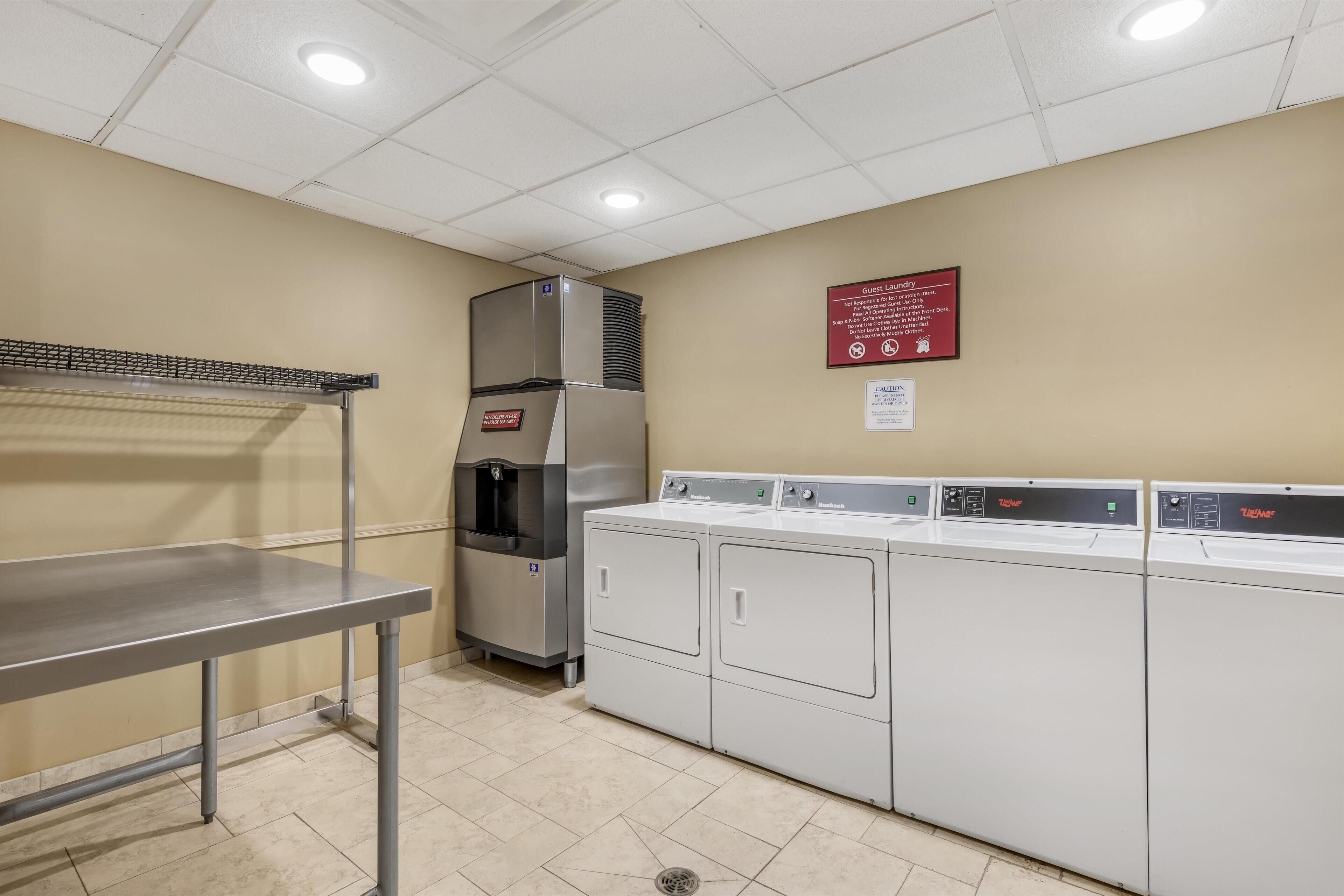 A laundry area with a stainless steel refrigerator, a water dispenser, and a row of white washers and dryers.