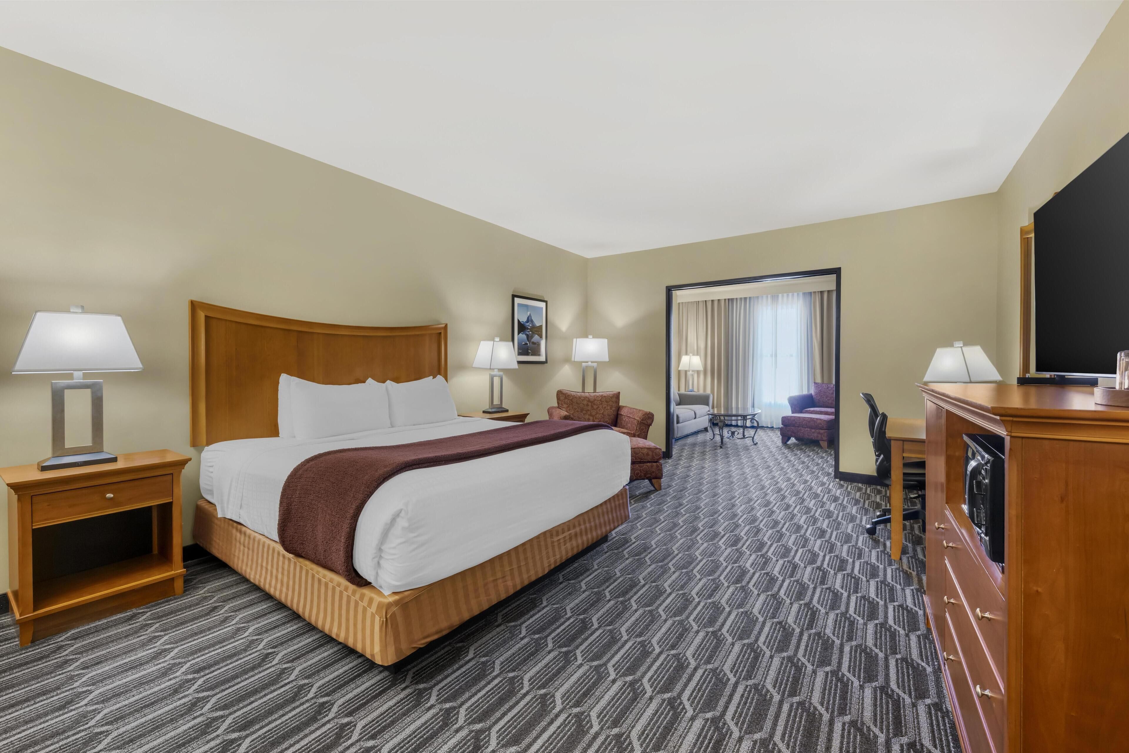 A hotel room with a large bed, two bedside tables with lamps, a desk with a chair, a television, and a mirror.
