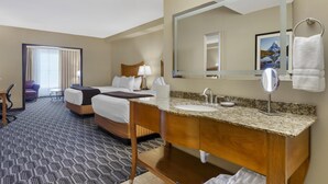 A hotel room with a large bed, a wooden vanity with a sink, a mirror, and a large window with curtains. - Best Western Plus Swiss Chalet Hotel & Suites (Pecos)
