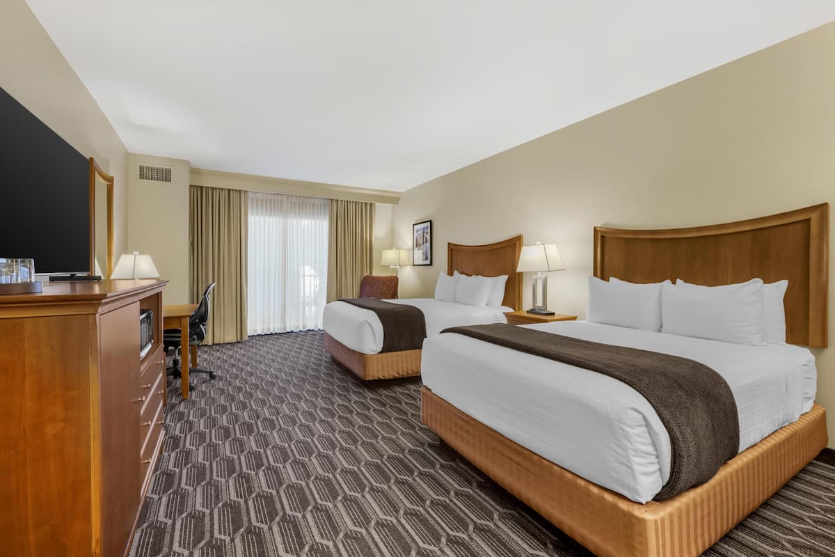 Een hotelkamer met twee bedden, een bureau, een televisie en een groot raam met gordijnen.