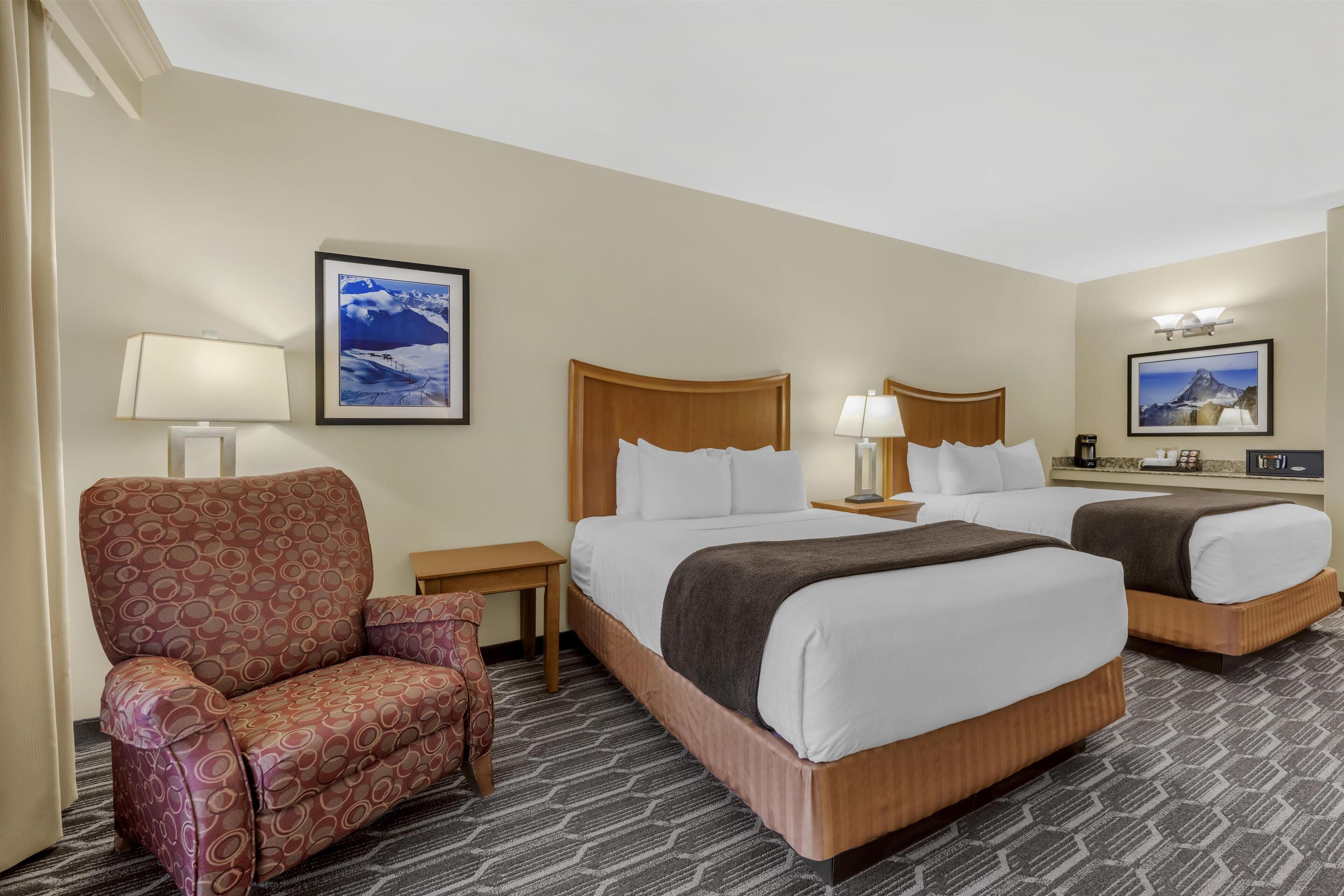 A hotel room with two beds, a sofa, a lamp, and framed pictures on the walls.