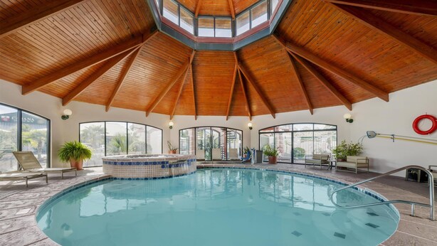 An indoor swimming pool with a wooden ceiling, large windows, and a hot tub area. - Best Western Plus Swiss Chalet Hotel & Suites (Pecos)