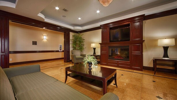 A lobby with a sofa, a coffee table, a fireplace, a television, and a plant. - Best Western Plus Manvel Inn & Suites (Manvel)
