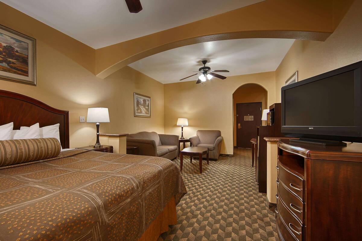 A hotel room with a large bed, a sofa, a TV, and a ceiling fan.