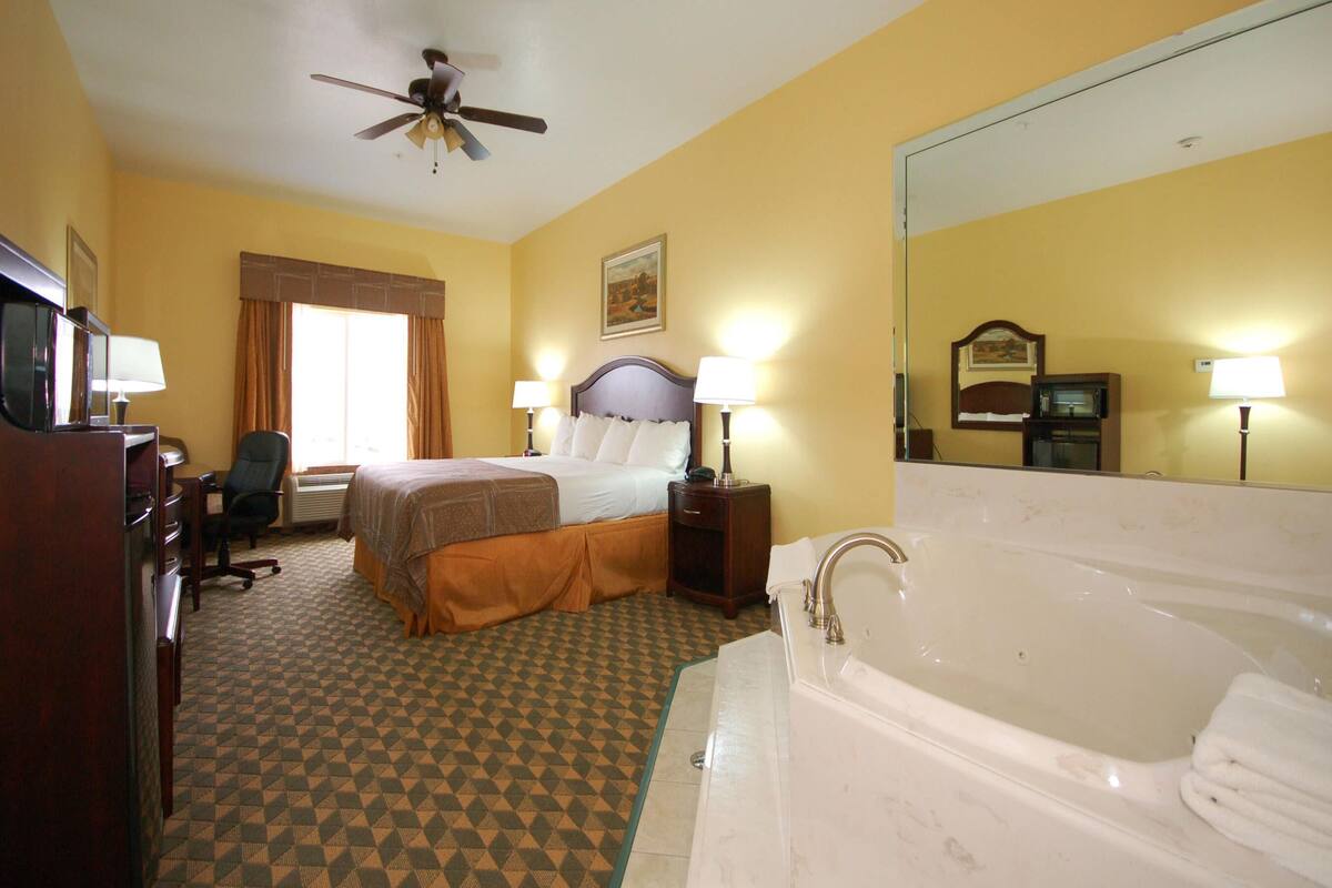 A hotel room with a bed, a desk, a chair, a desk lamp, a floor lamp, a ceiling fan, and a bathtub.