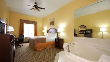 A hotel room with a bed, a desk, a chair, a desk lamp, a floor lamp, a ceiling fan, and a bathtub.