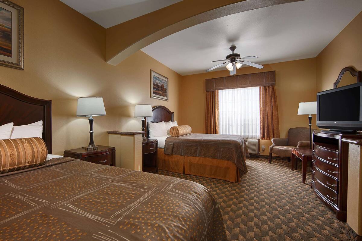 A hotel room with two beds, a television, a desk, and a ceiling fan.