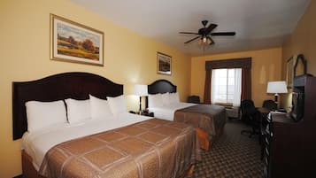 A hotel room with two beds, a ceiling fan, a desk with a chair, a TV, and a window with curtains.