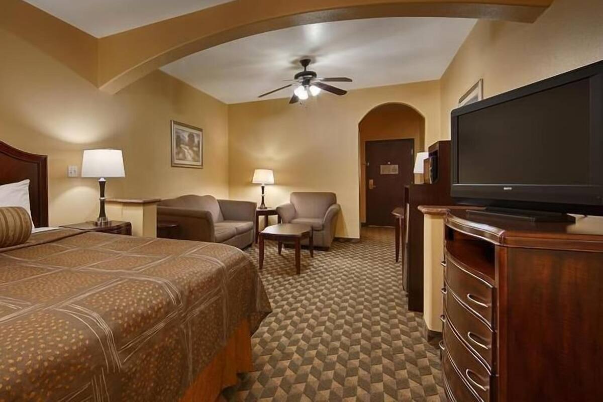 A hotel room with a bed, a TV, a ceiling fan, a desk, and a chair.