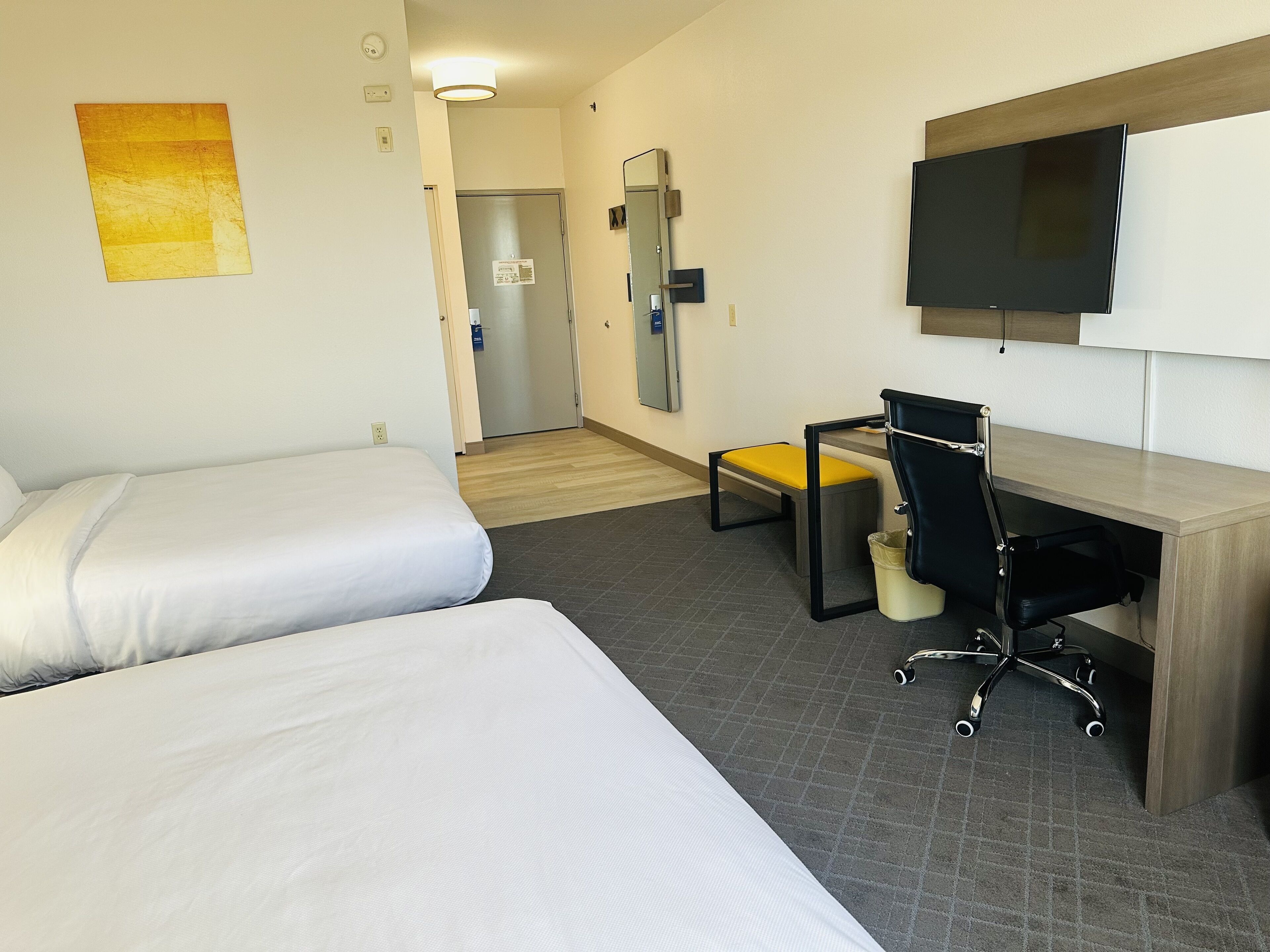 A hotel room with two single beds, a desk with a chair, a television, and a small trash bin.