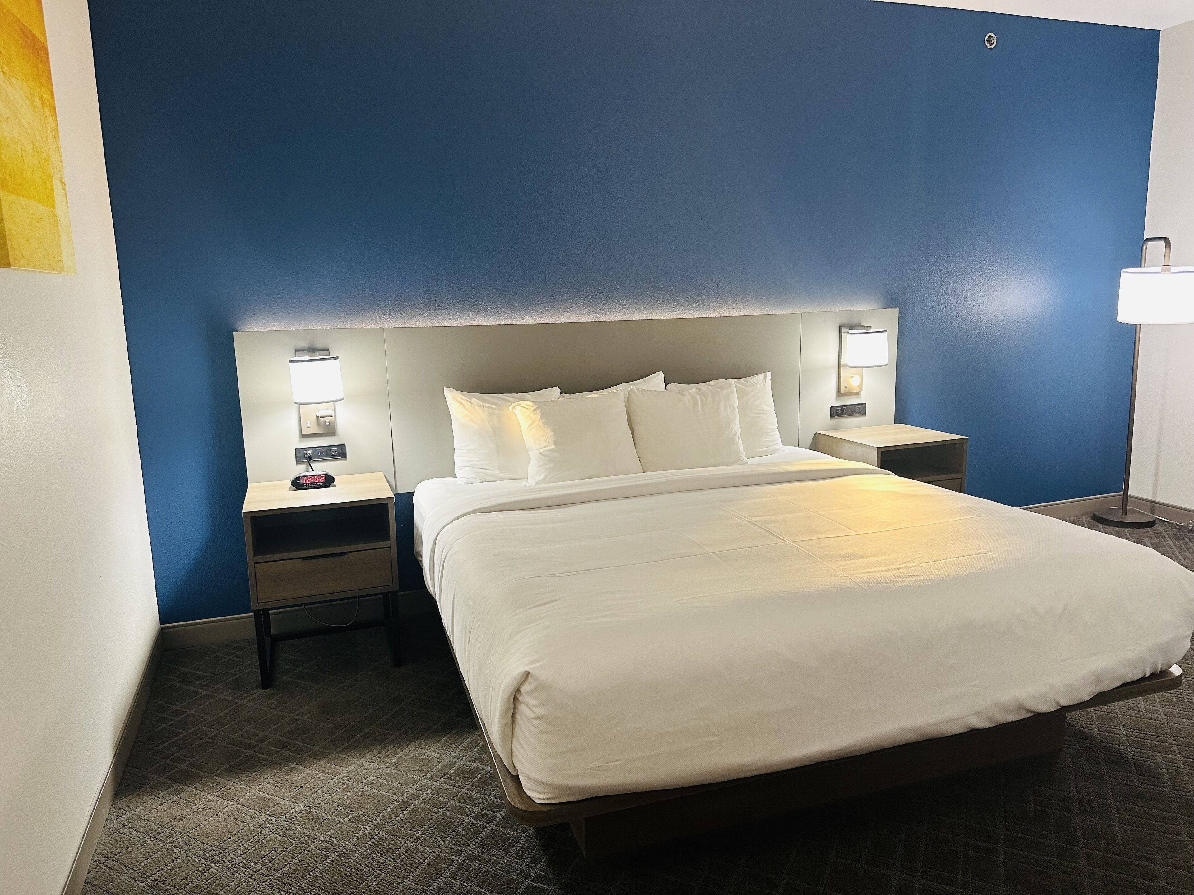 A hotel room with a large bed, two bedside tables with lamps, and a blue accent wall.