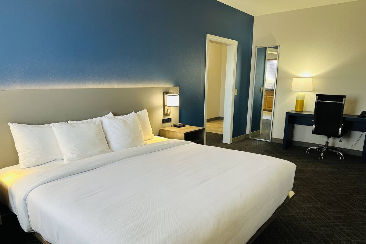 Une chambre d’hôtel avec un grand lit, des tables de chevet, un bureau avec une chaise et un miroir.