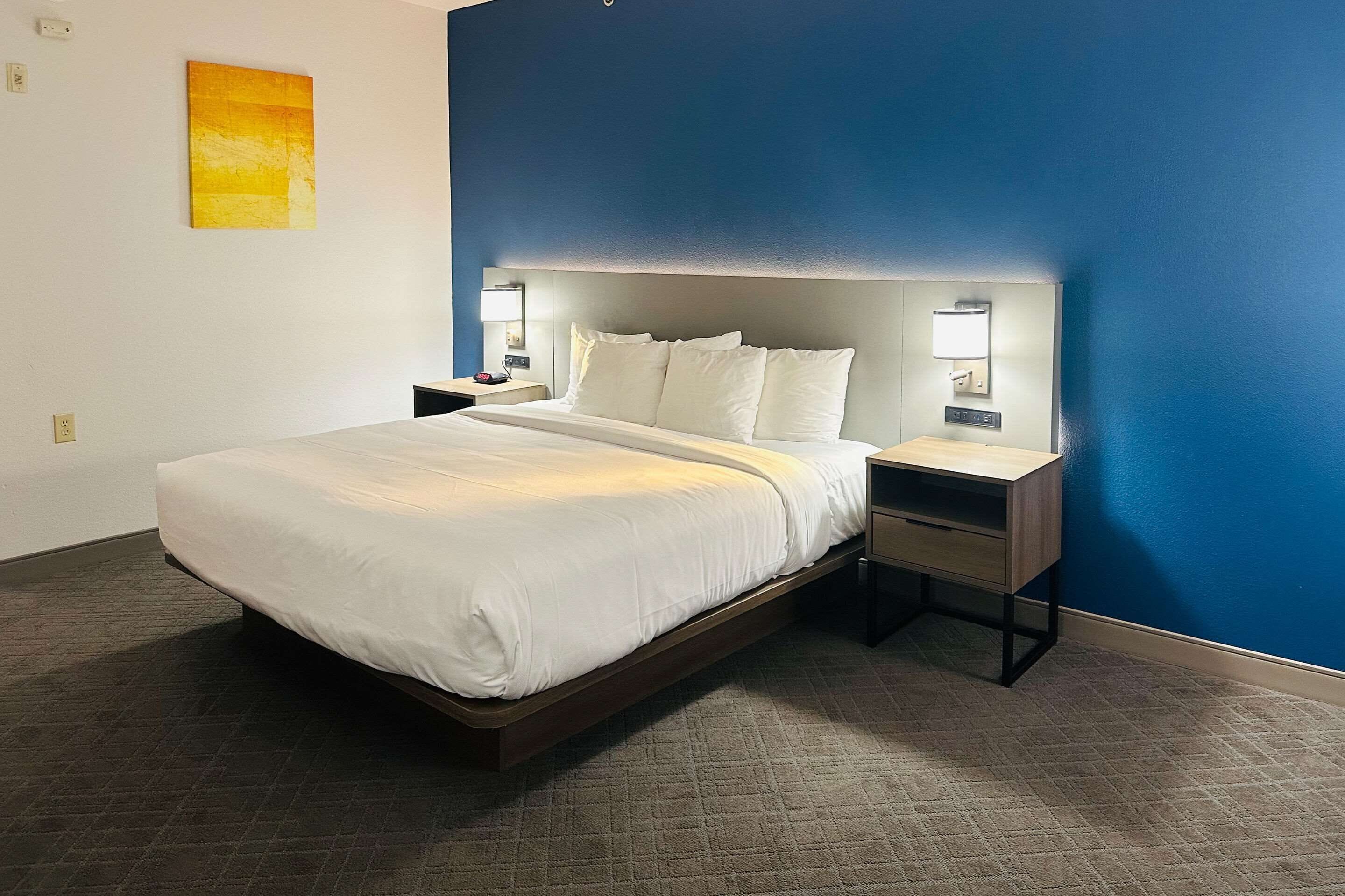 Une chambre d’hôtel moderne avec un grand lit, des tables de chevet et un mur d’accent bleu.