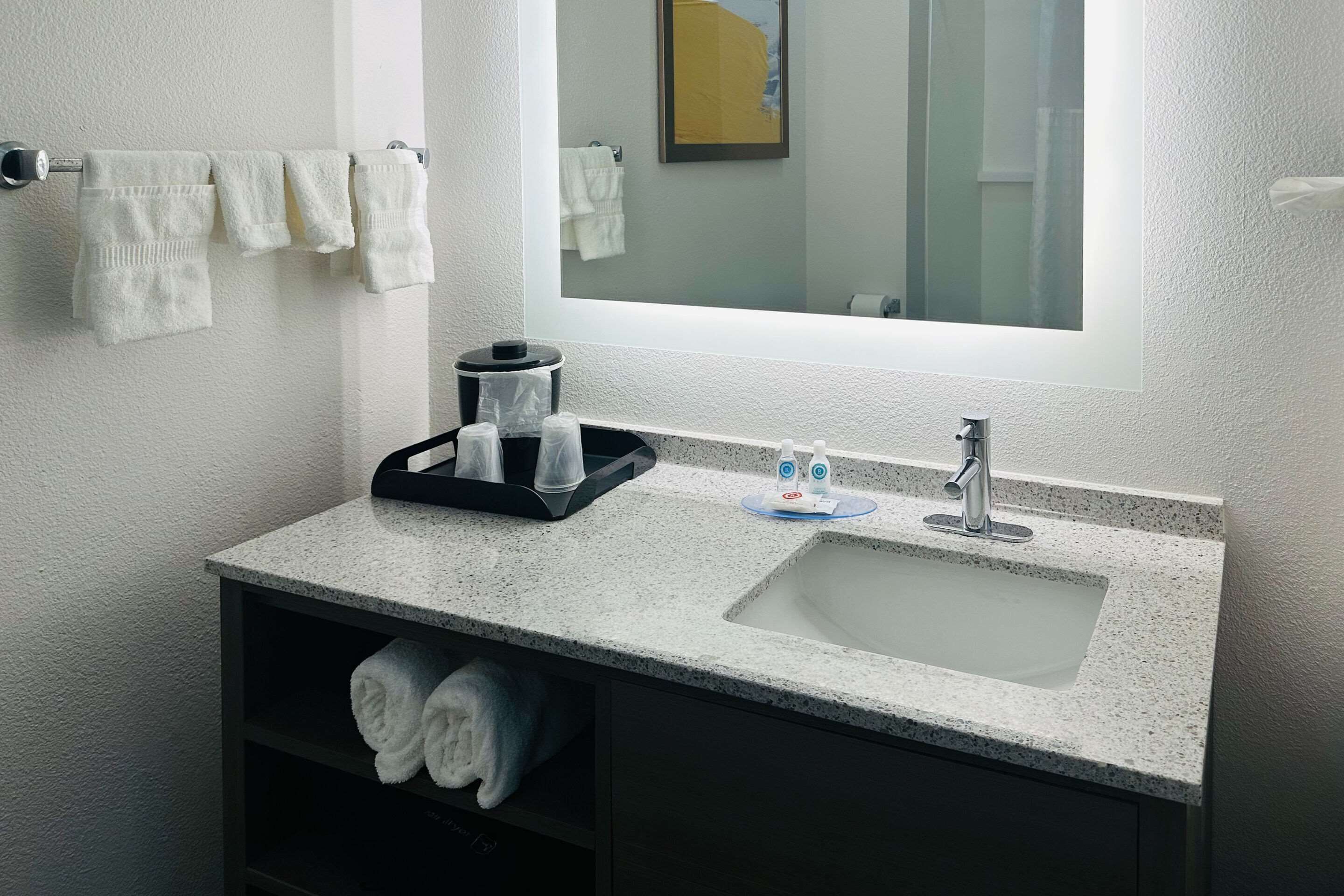 A bathroom with a granite countertop sink, a mirror above it, and towels hanging on a rack.